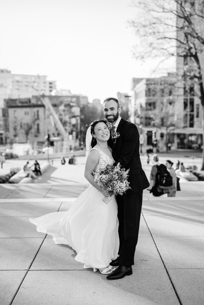 Bride and groom embracing outdoors after their courthouse wedding ceremony with a city backdrop behind them.