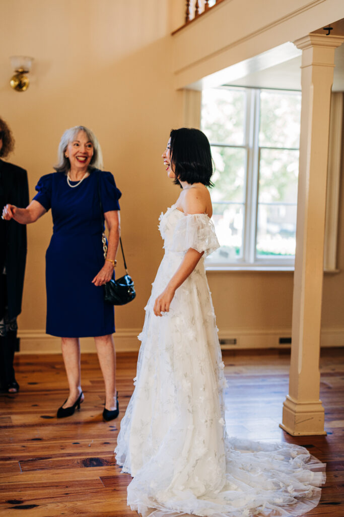 Bride in an off-the-shoulder floral wedding dress greeting guests inside the ceremony space.