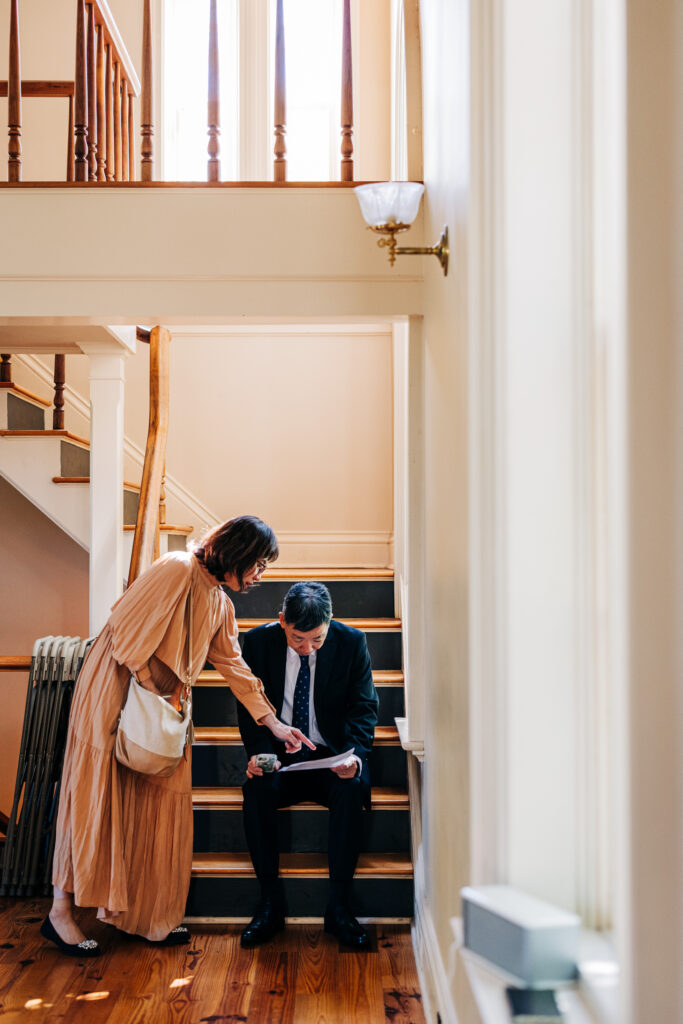 Two guests reviewing ceremony papers while seated on a wooden staircase inside the venue.