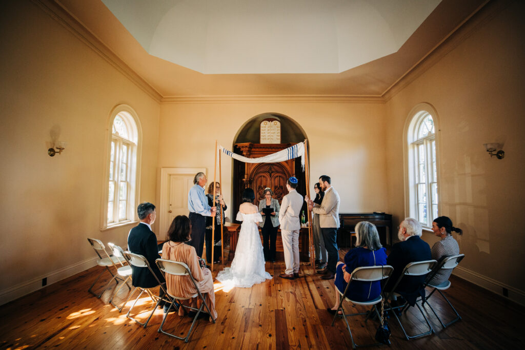 Wide view of the wedding ceremony beneath a chuppah inside Gates of Heaven in Madison.