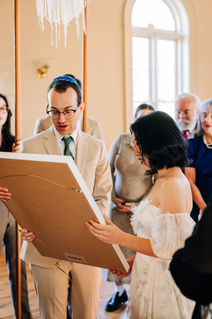 Bride and groom examining a framed marriage document during the ceremony.