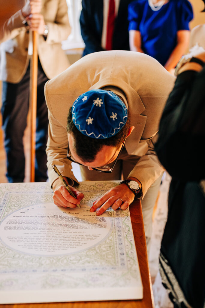 Groom signing the marriage document beneath the wedding canopy.
