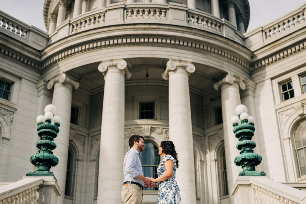 Couple holding hands in front of the Wisconsin State Capitol during their downtown Madison engagement session.