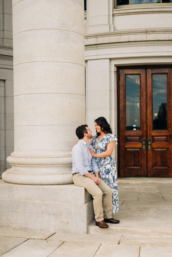 Couple embracing beside a large stone column outside the Wisconsin State Capitol in downtown Madison.