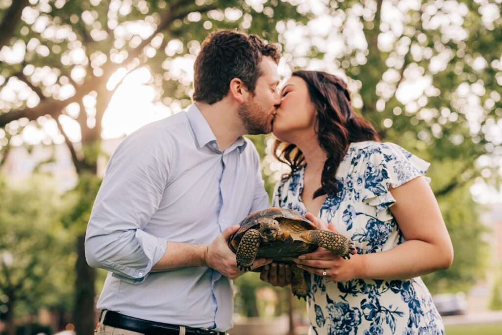 Couple sharing a kiss while holding their tortoise during a playful downtown Madison engagement session.
