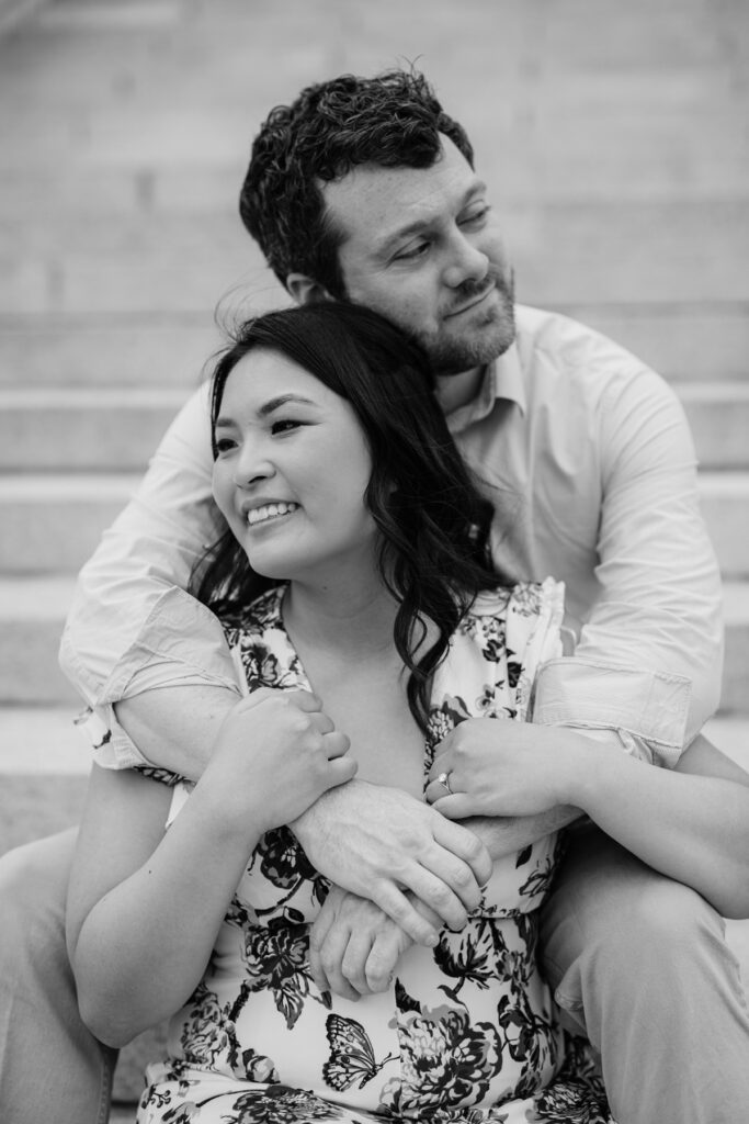 Black-and-white portrait of an engaged couple embracing on stone steps during their engagement session.