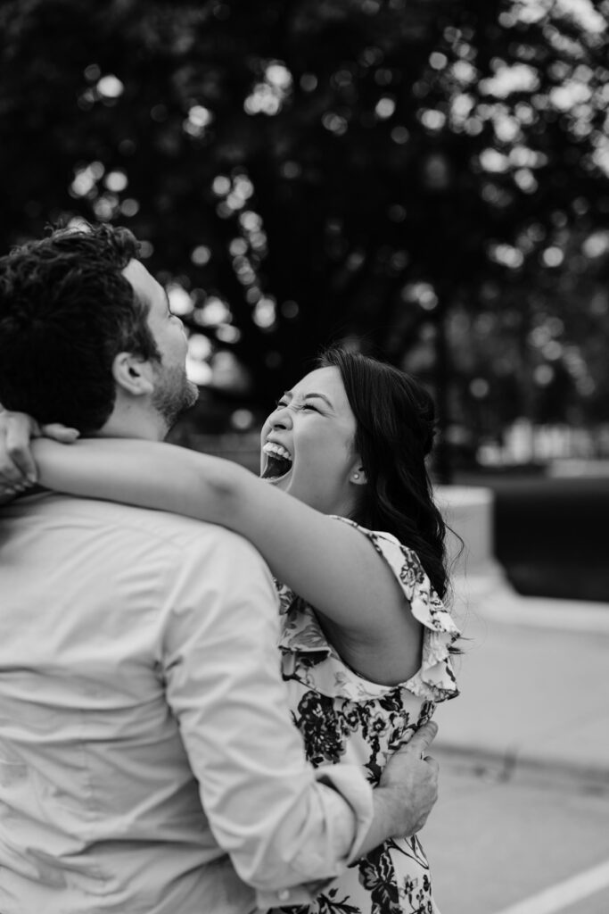 Black-and-white candid of an engaged couple laughing together during an outdoor engagement session.