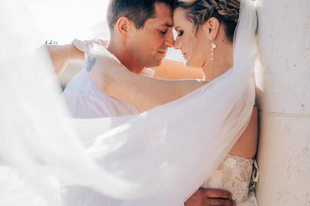 Close portrait of the couple resting forehead to forehead as the bride's veil catches the afternoon breeze.