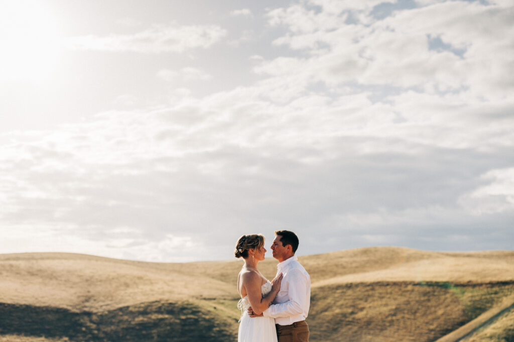 Bride and groom embrace against rolling hills during golden hour wedding portraits.