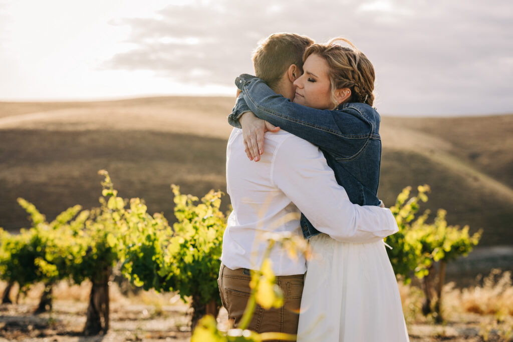 Bride embracing groom in a sunlit vineyard during an intimate outdoor wedding portrait at sunset.