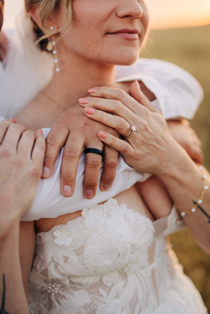 Close-up of the bride's engagement ring and couple's hands during a romantic embrace at sunset.