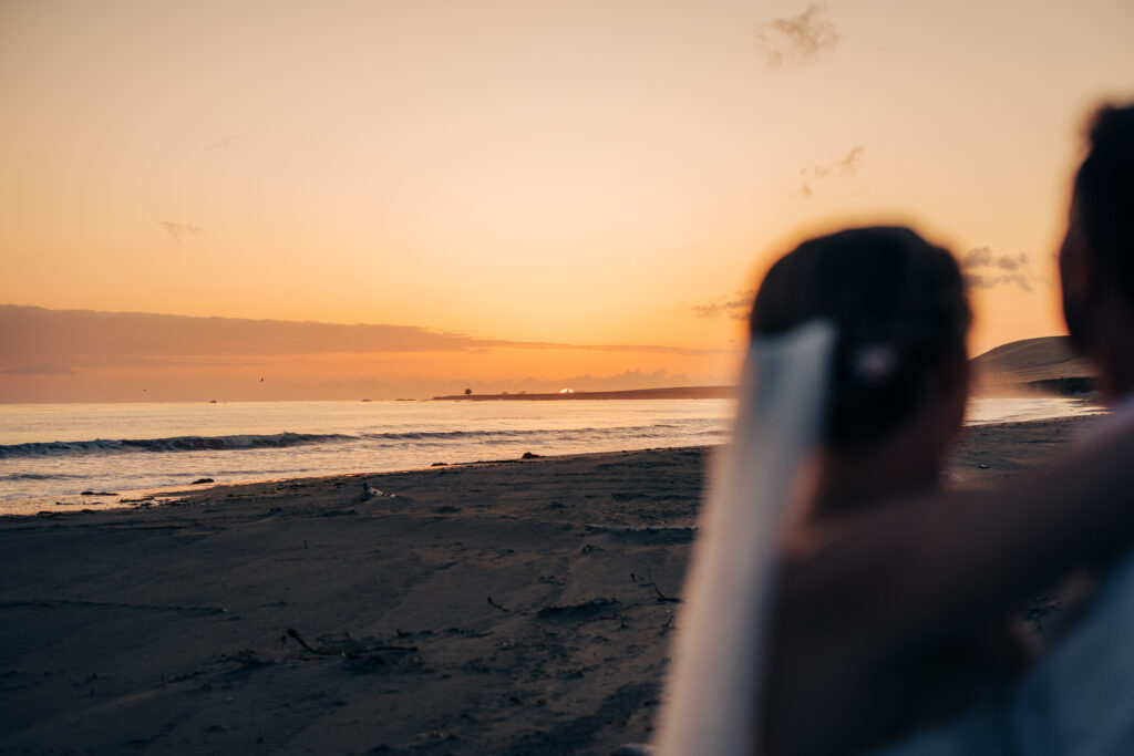 Bride and groom watching the sunset over the ocean on a peaceful sandy beach.
