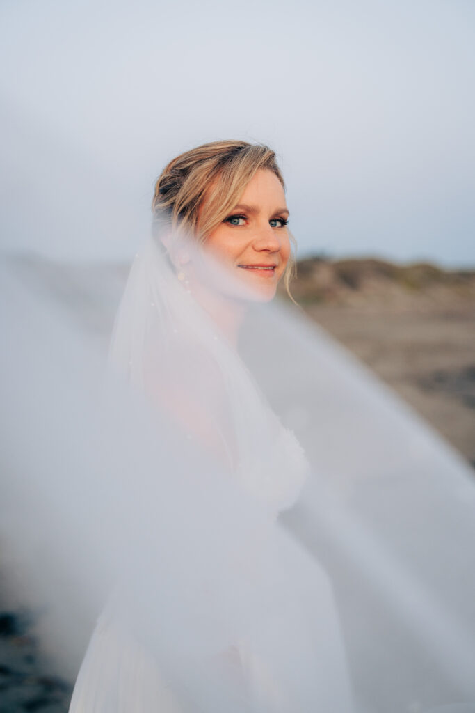 Bride smiling through a flowing veil during a beach wedding portrait at San Simeon Beach.
