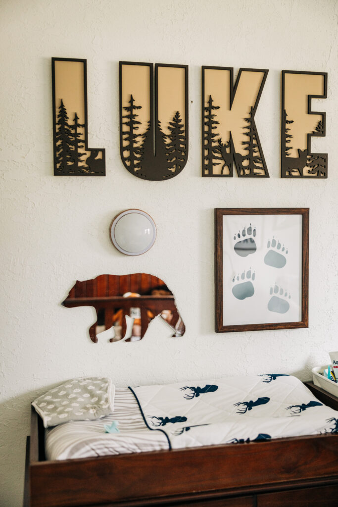 Woodland-themed nursery with a personalized name sign, bear artwork, and changing table prepared for a newborn at home