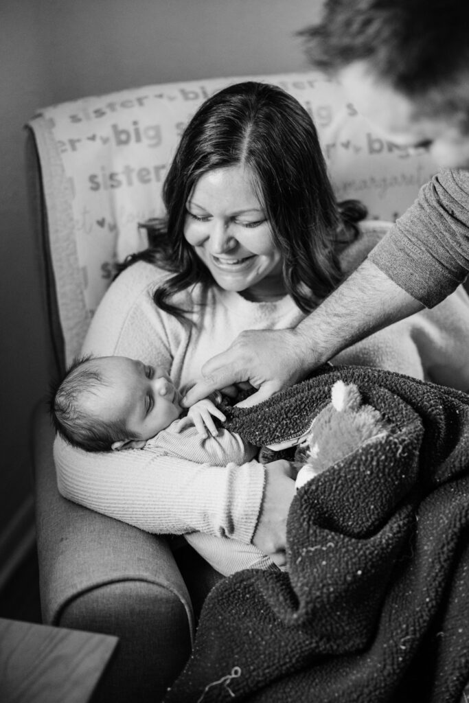 Mother smiles down at her newborn while another hand gently adjusts the baby's blanket.