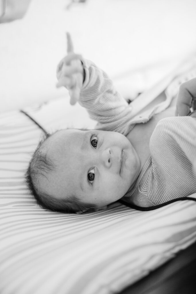 Awake newborn looks toward the camera while lying on a striped changing pad.