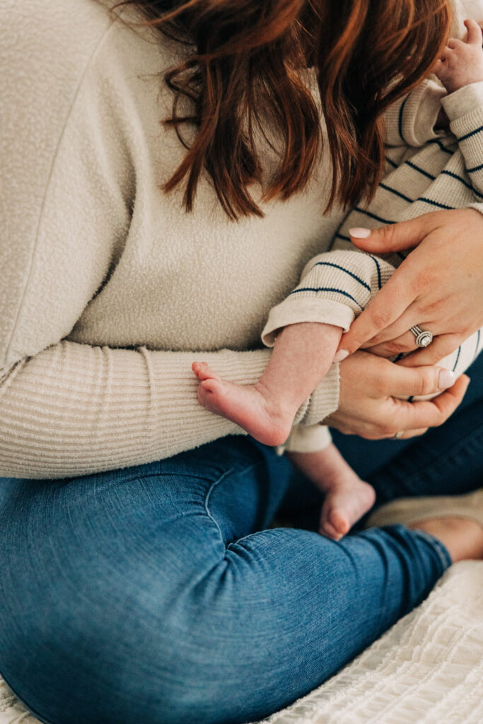 Close-up of a mother cradling a newborn, highlighting tiny feet and gentle hands during an in-home newborn session.