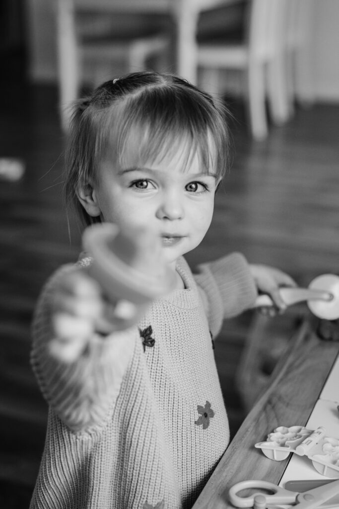 Toddler reaches toward the camera while playing at a table during a candid in-home family photography session.