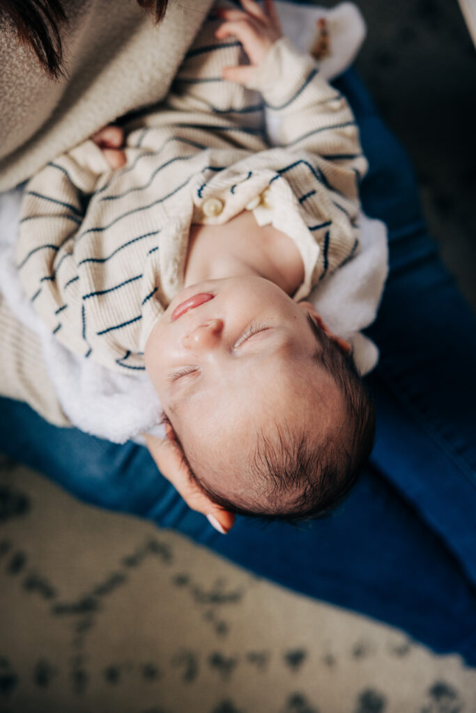 Close-up of a sleeping newborn cradled in an adult’s arms and wearing a striped outfit.
