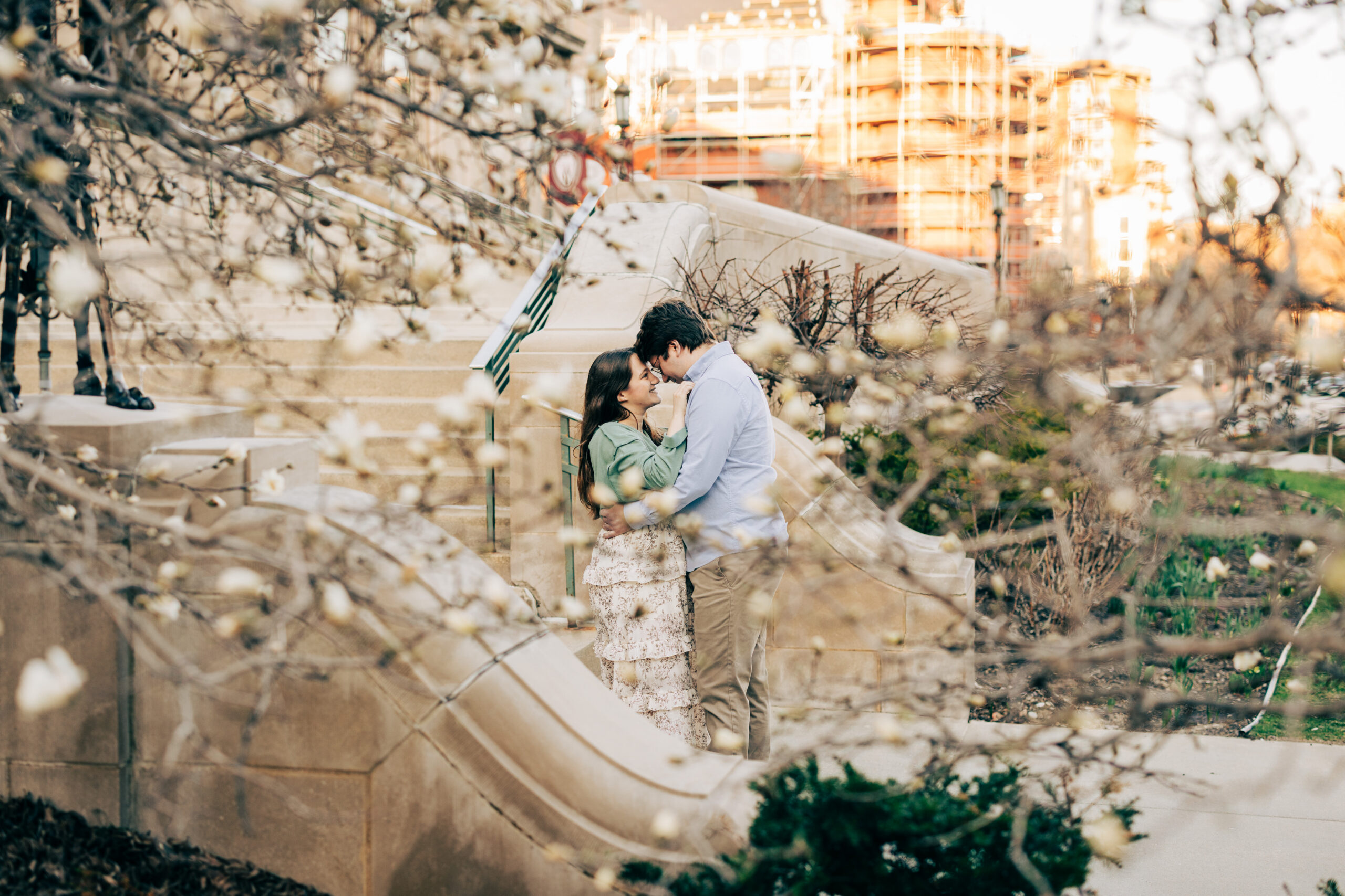 Couple embracing in a blooming garden with flowering branches framing the portrait.